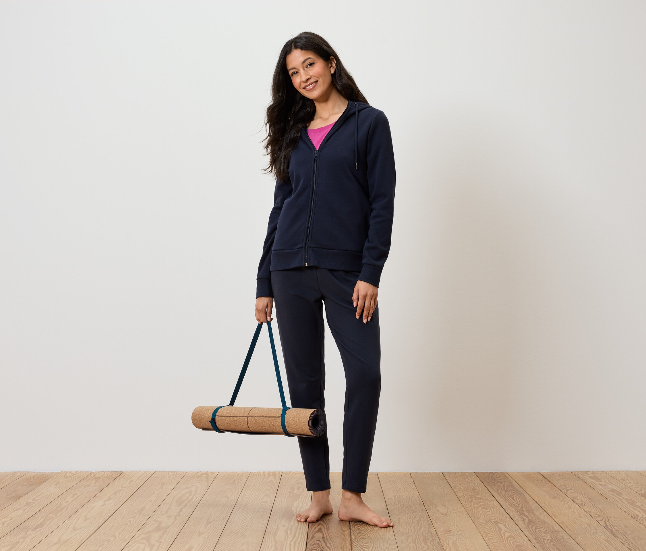 Žena drží podložku na cvičenie jogy, oblečená v tmavomodrej súprave a ružovom tielku.