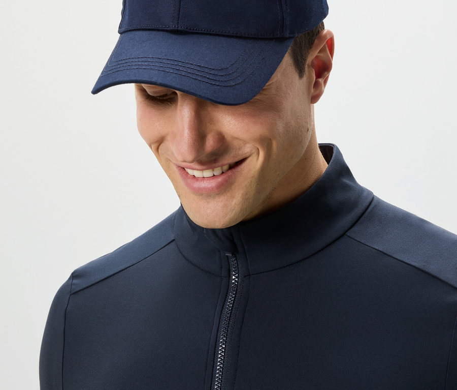 Muž v tmavomodrej funkčnej bunde a čiapke sa pozerá dole.