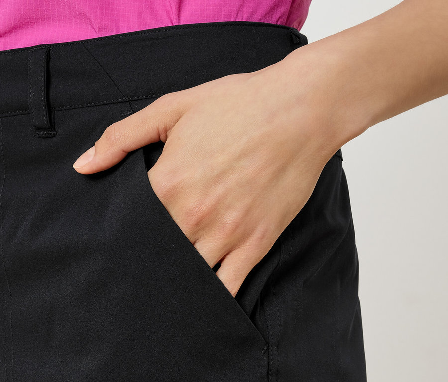 Žena s rukou vo vrecku čiernych nohavíc a ružovou košeľou.