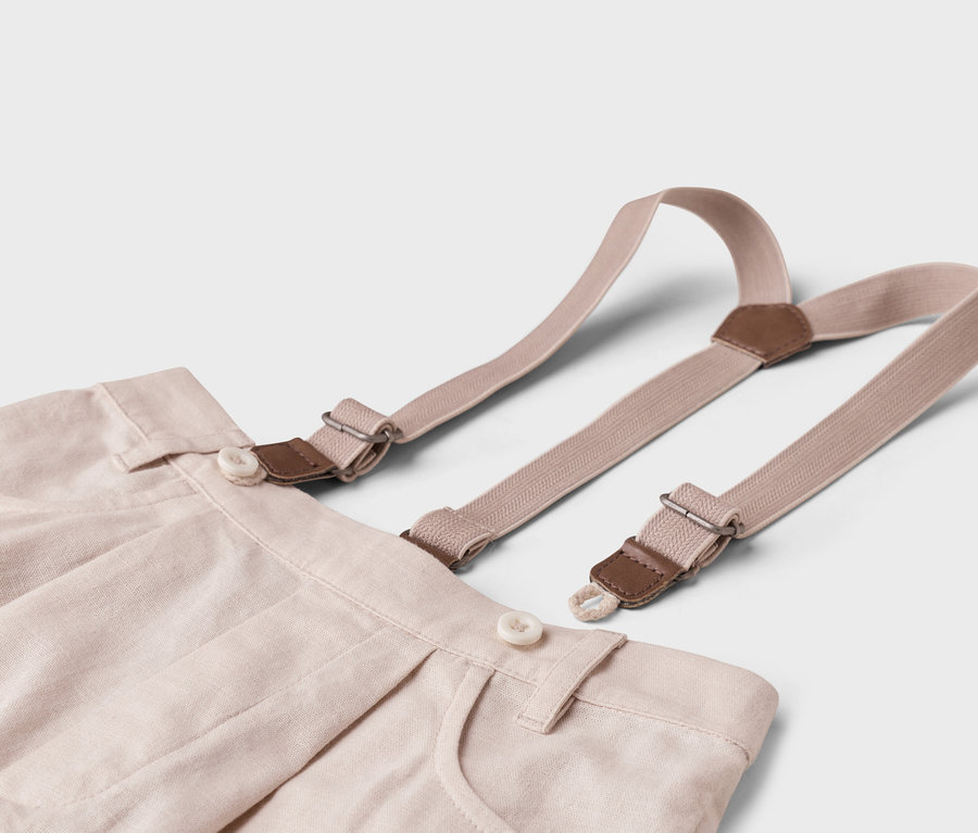 Detail béžových látkových nohavíc s trakmi na bielom pozadí.