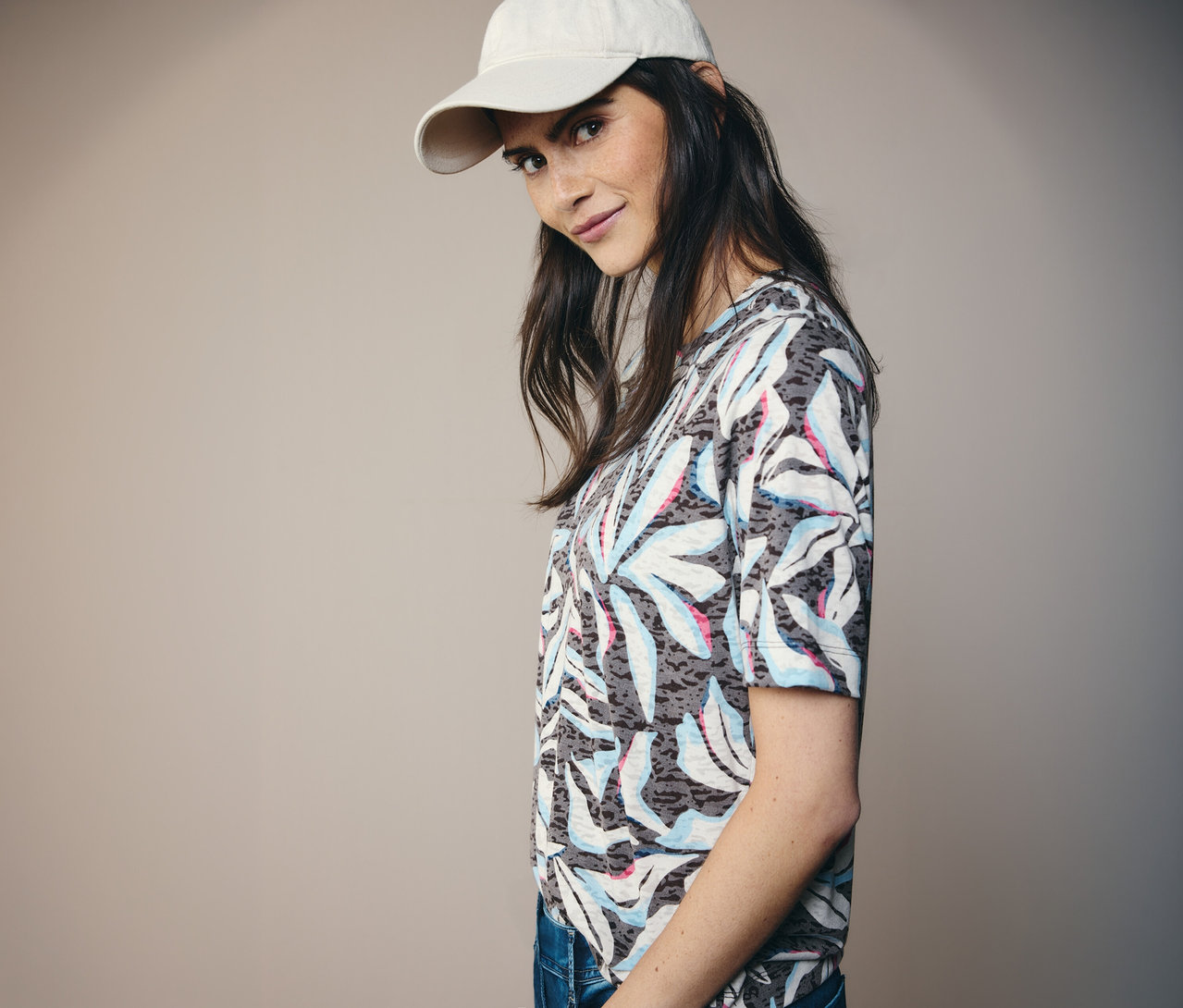 Žena v béžovej šiltovke a modrom tričku s krátkym rukávom CECIL s potlačou listov.