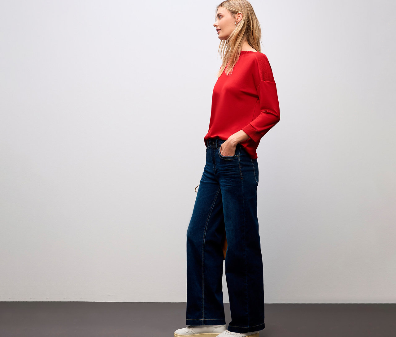 Žena v červenom tričku Street One s rebrovanými detailmi a v džínsoch.