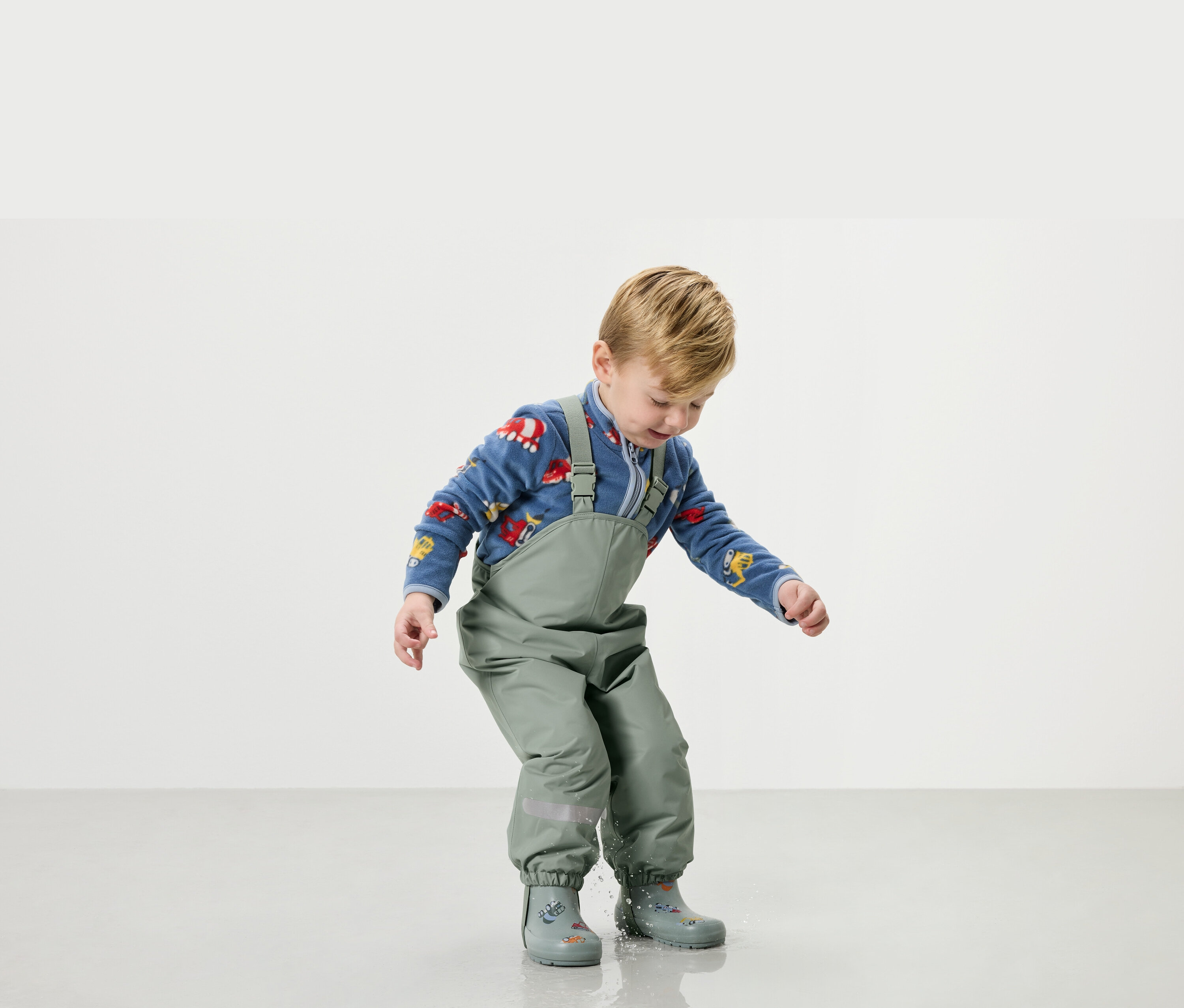 Chlapec sa hrá vo vode v zelenom daždiaku a gumákoch.