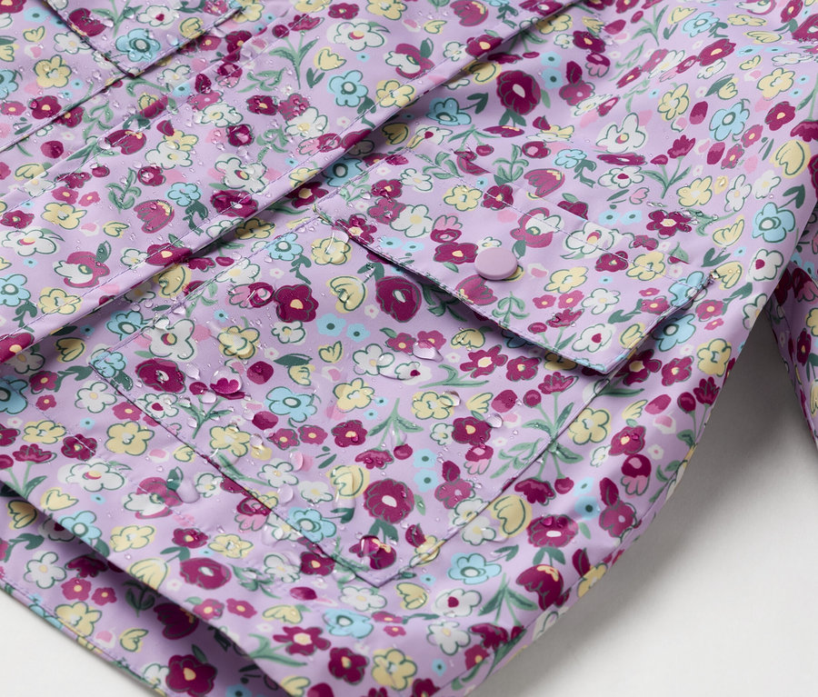 Detail fialovej pláštenky s kvetinovou potlačou a našitými vreckami zapínanými na gombíky.