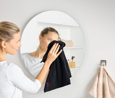 Žena čistí zahmlené okrúhle zrkadlo čiernou handričkou.