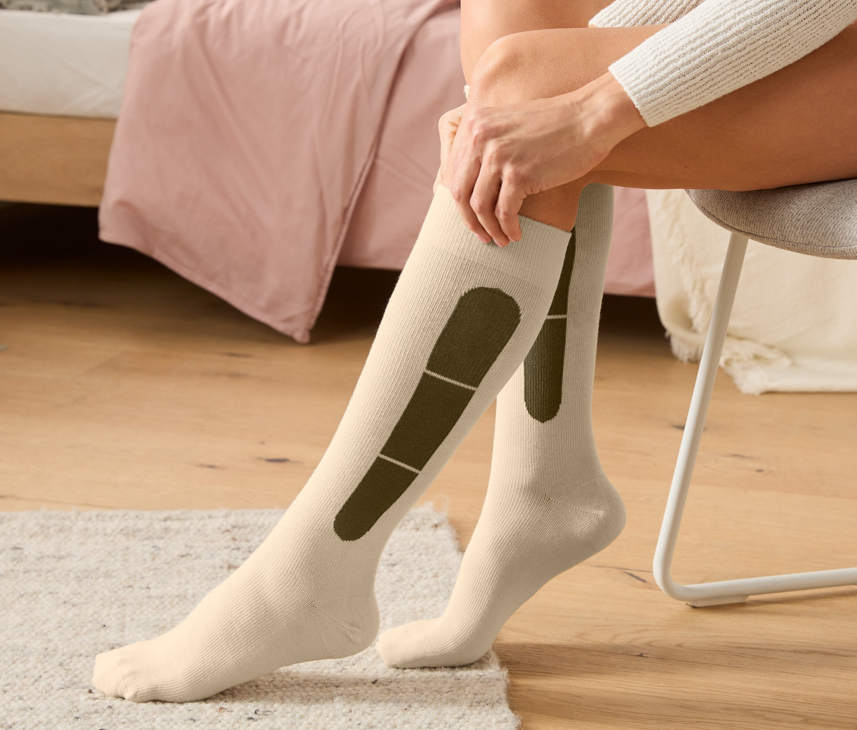 Žena sedí na stoličke a naťahuje si béžové cestovné kompresné podkolienky.