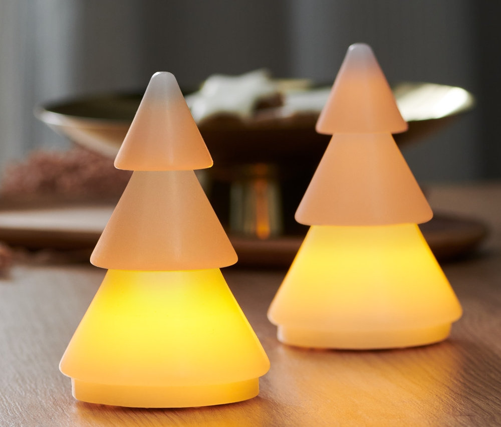 Dve jedličky z pravého vosku s LED stoja na drevenom stole. V pozadí je okno.