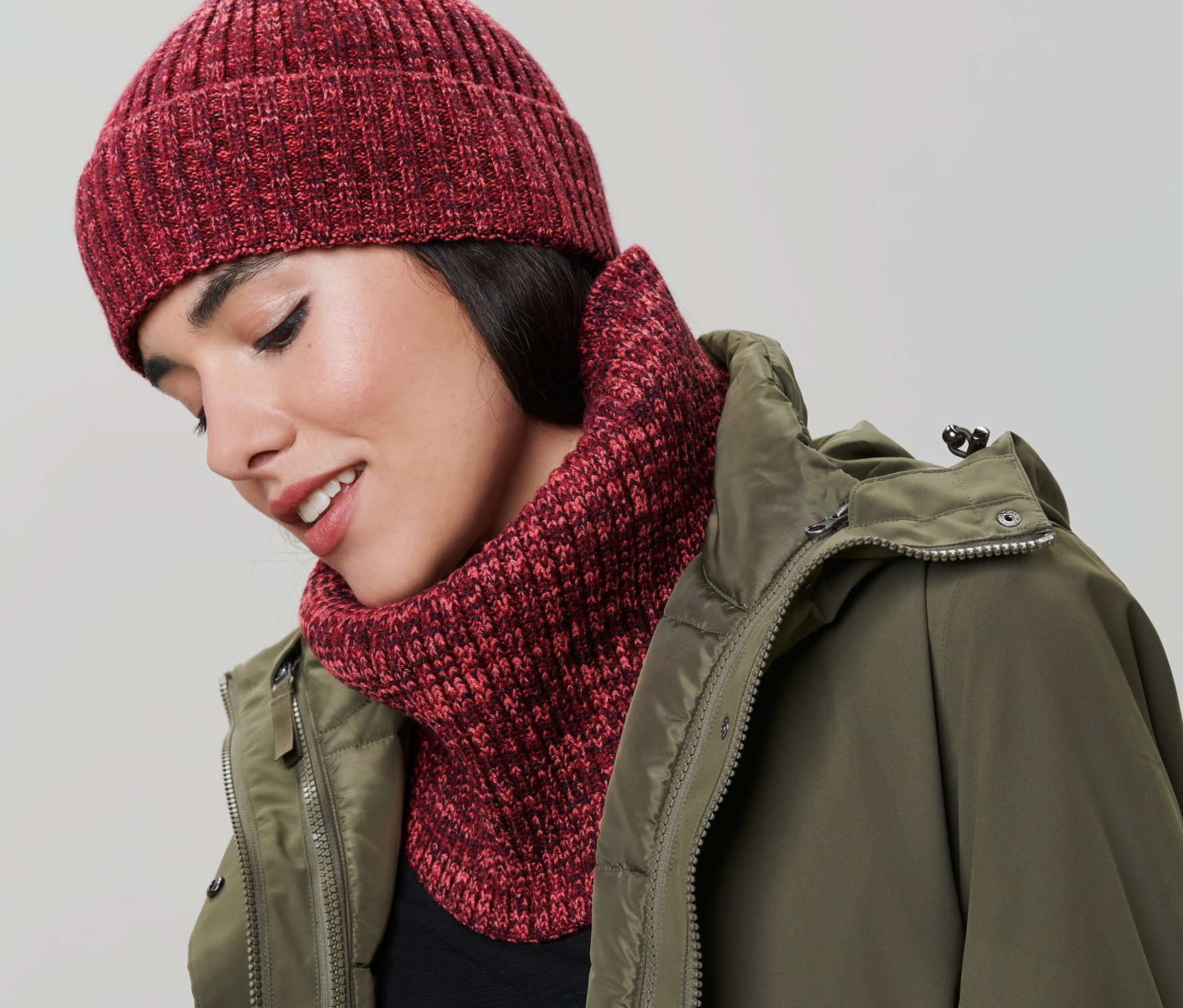 Žena nosí pletený kruhový šál a čiapku. Má na sebe zelenú bundu.
