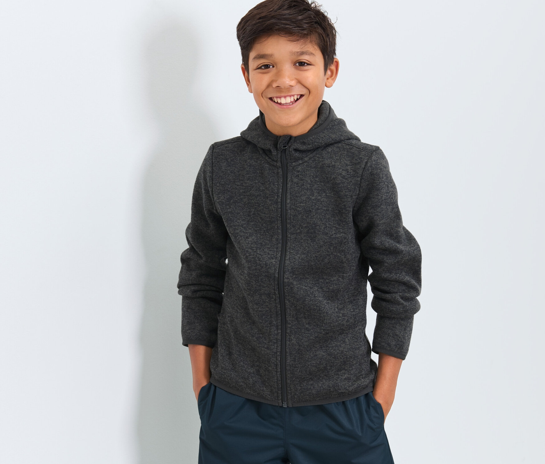 Chlapec má na sebe detskú bundu z pleteného flaušu a tmavomodré nohavice.