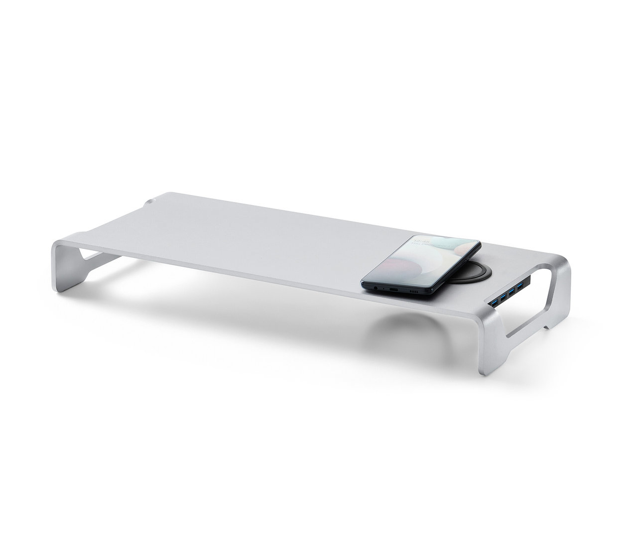 Strieborný stojan na monitor s bezdrôtovou nabíjacou stanicou a USB hubom. Na nabíjacej stanici leží mobilný telefón.