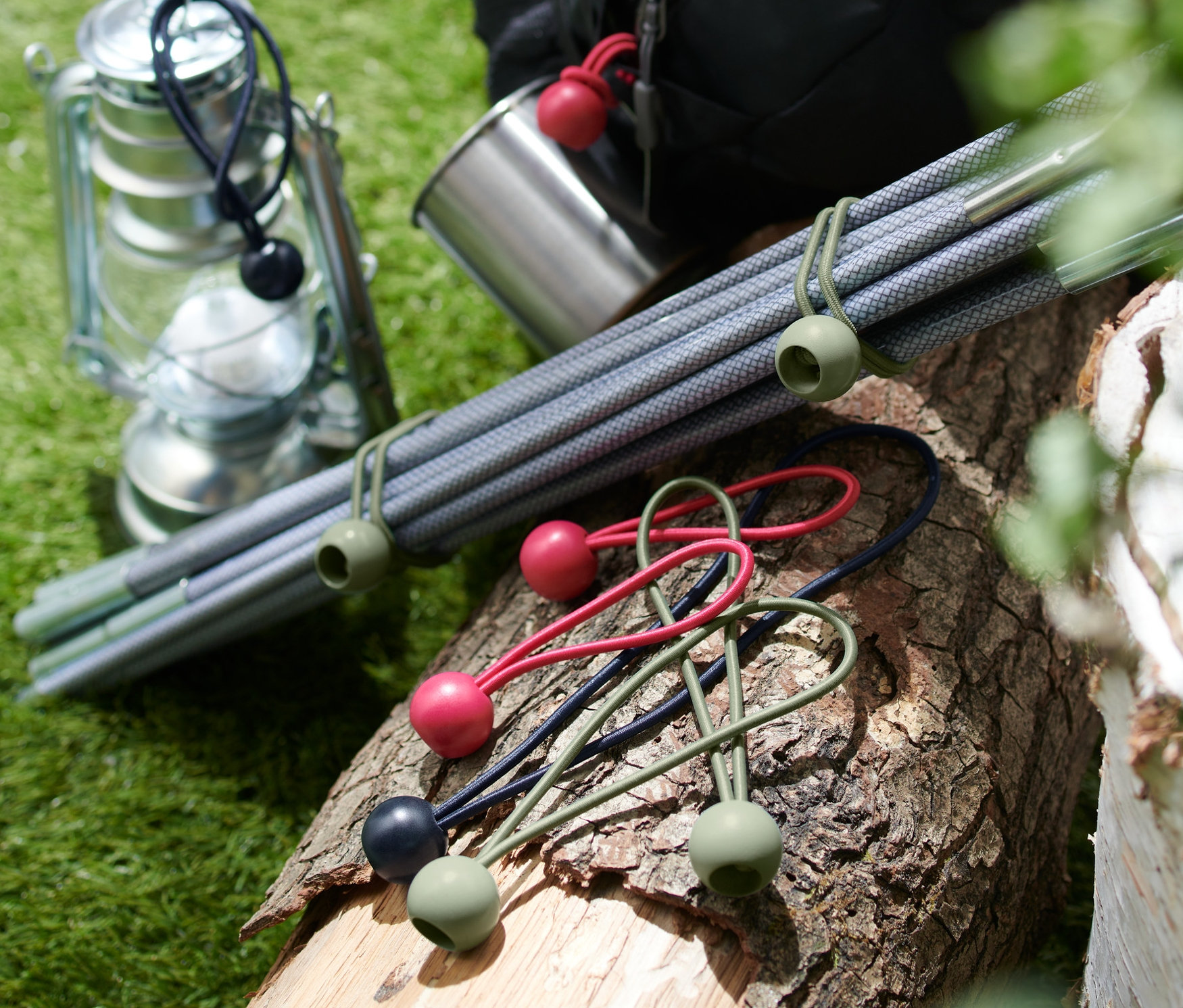 Na klade leží 12 napínacích gúm s guľôčkou, vedľa nich je lampáš, kovový hrnček, tyče a batoh.