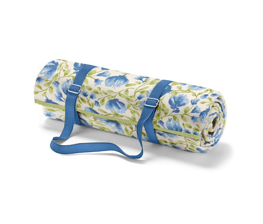 Zrolovaná malá pikniková deka s modrými kvetmi a zelenými stonkami, upevnená modrými popruhmi.