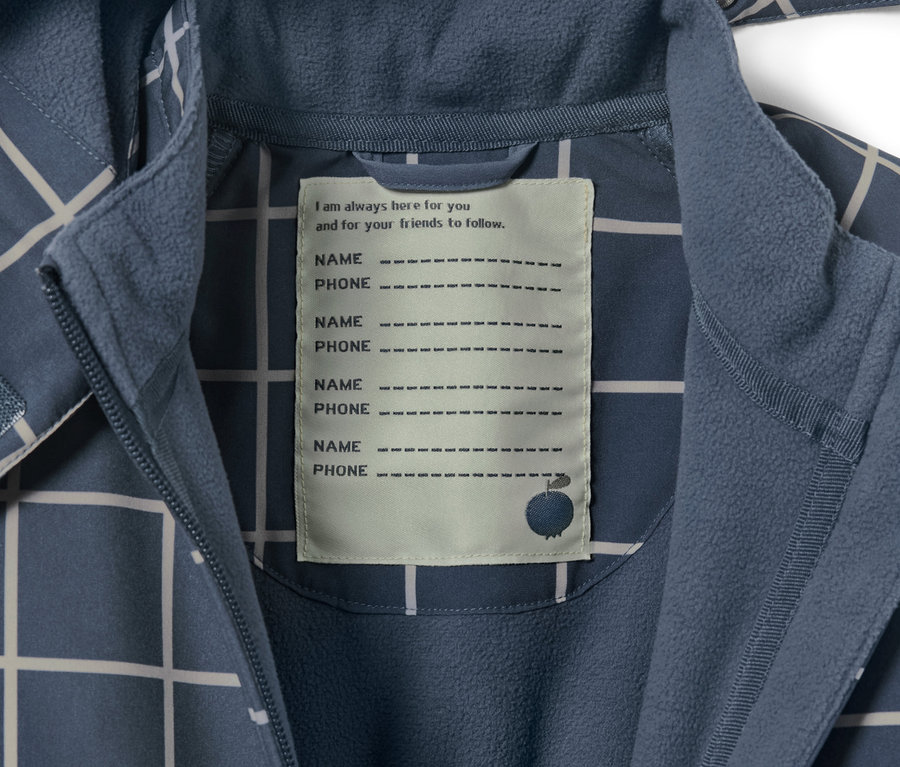 Detail detského softshellového overalu s kockovaným vzorom a štítkom na meno a telefónne číslo.