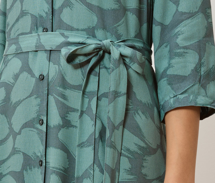 Detail tyrkysových košeľových šiat so sivým vzorom ťahov štetcom a zaviazaným pásom.