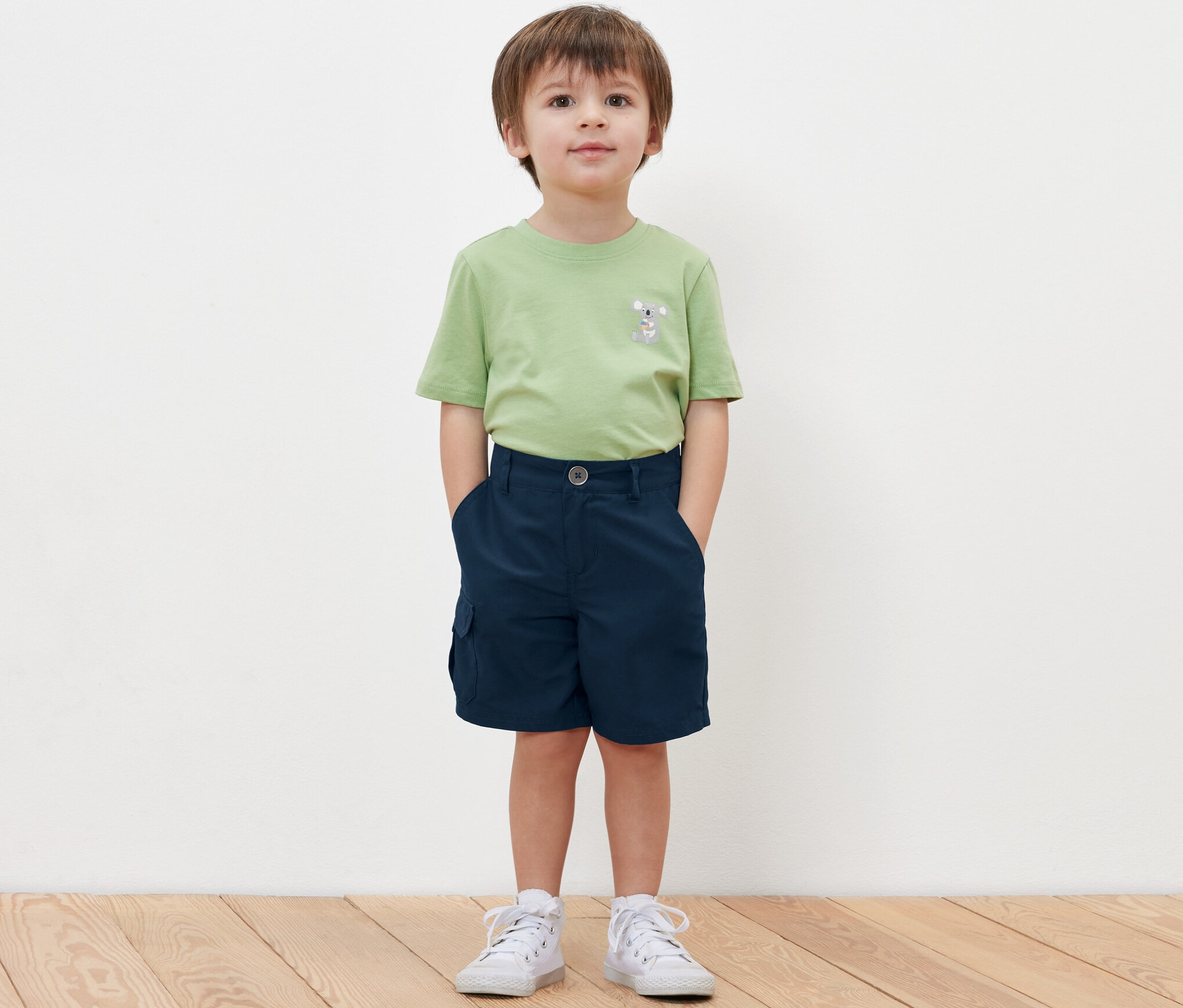 Chlapec stojí a má ruky vo vreckách detských funkčných šortiek.