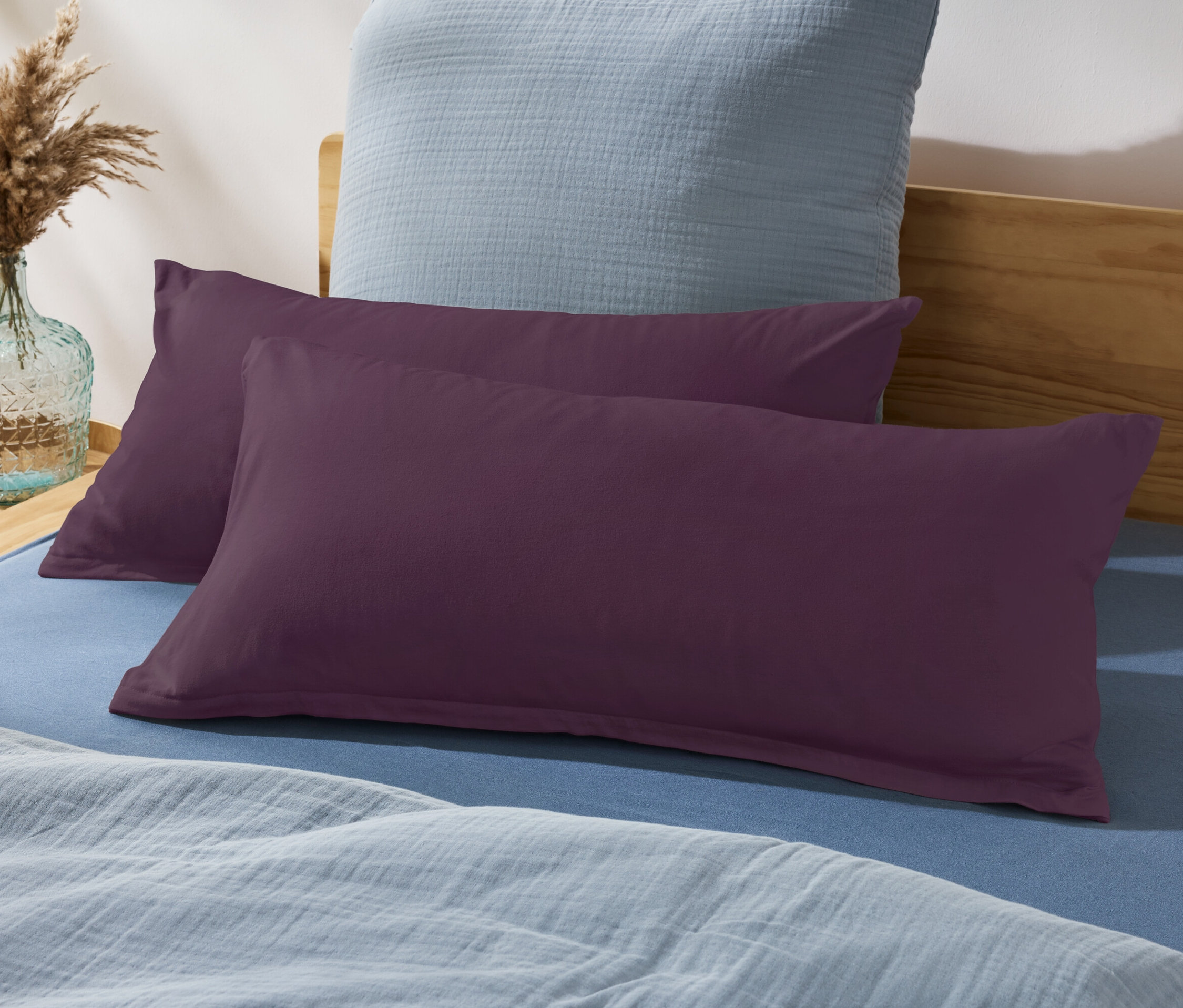 Dva fialové vankúše na posteli s modrou plachtou a modrým vankúšom v pozadí.