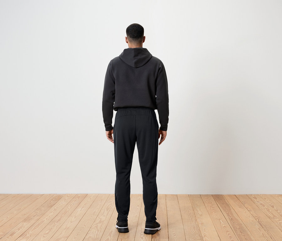 Muž chrbtom ku kamere má na sebe čierne nohavice a mikinu s kapucňou.