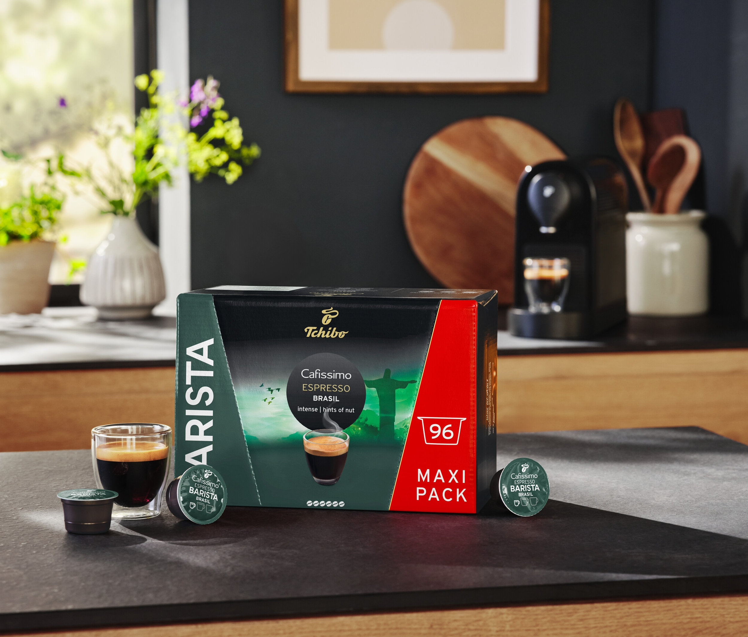 Na stole stojí balenie kapsúl Cafissimo BARISTA Espresso Brasil, pohár espressa a kávovar.