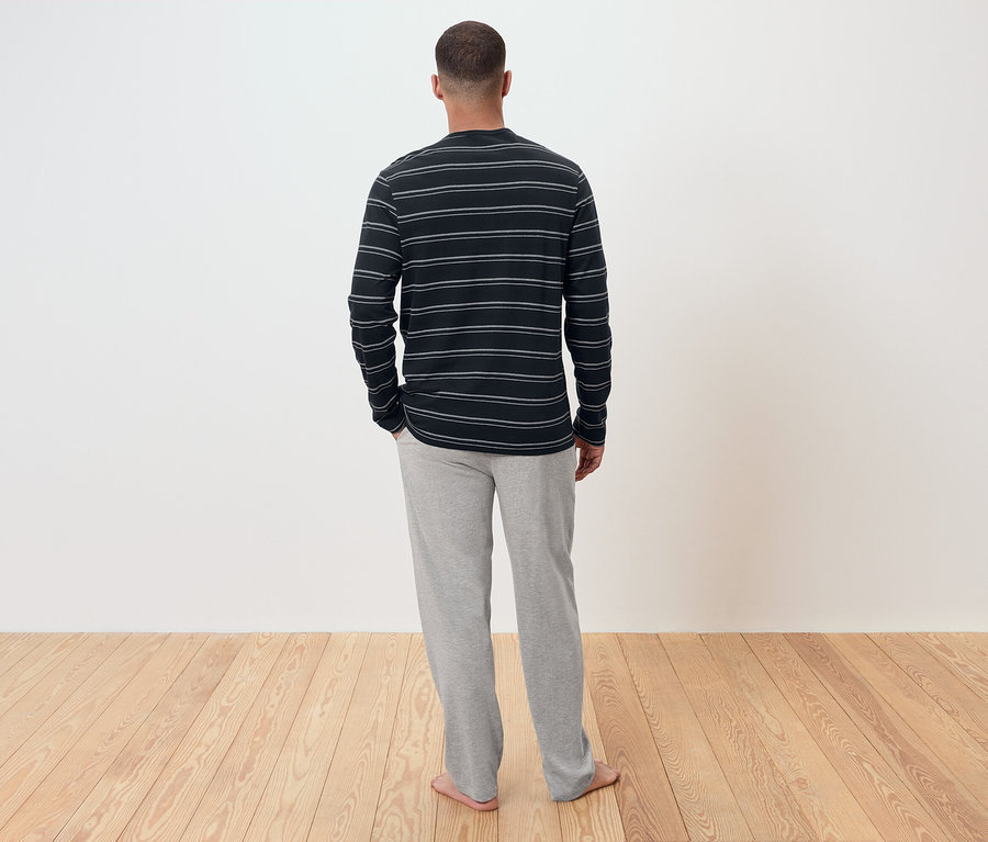 Muž chrbtom k fotoaparátu má na sebe pruhované tričko s dlhým rukávom a sivé tepláky.