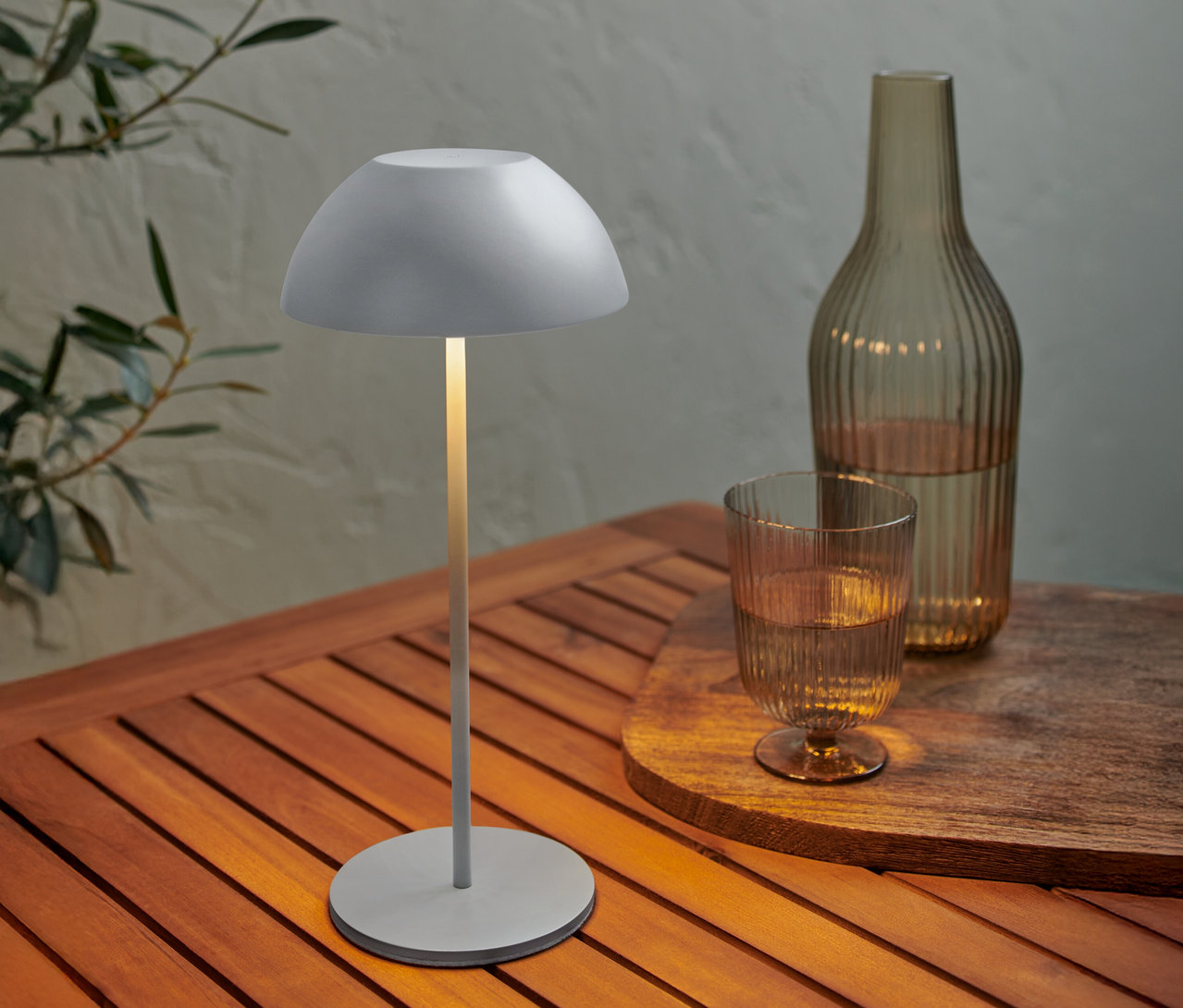 Na drevenom stole stojí sivá lampa vedľa fľaše a pohára vody.