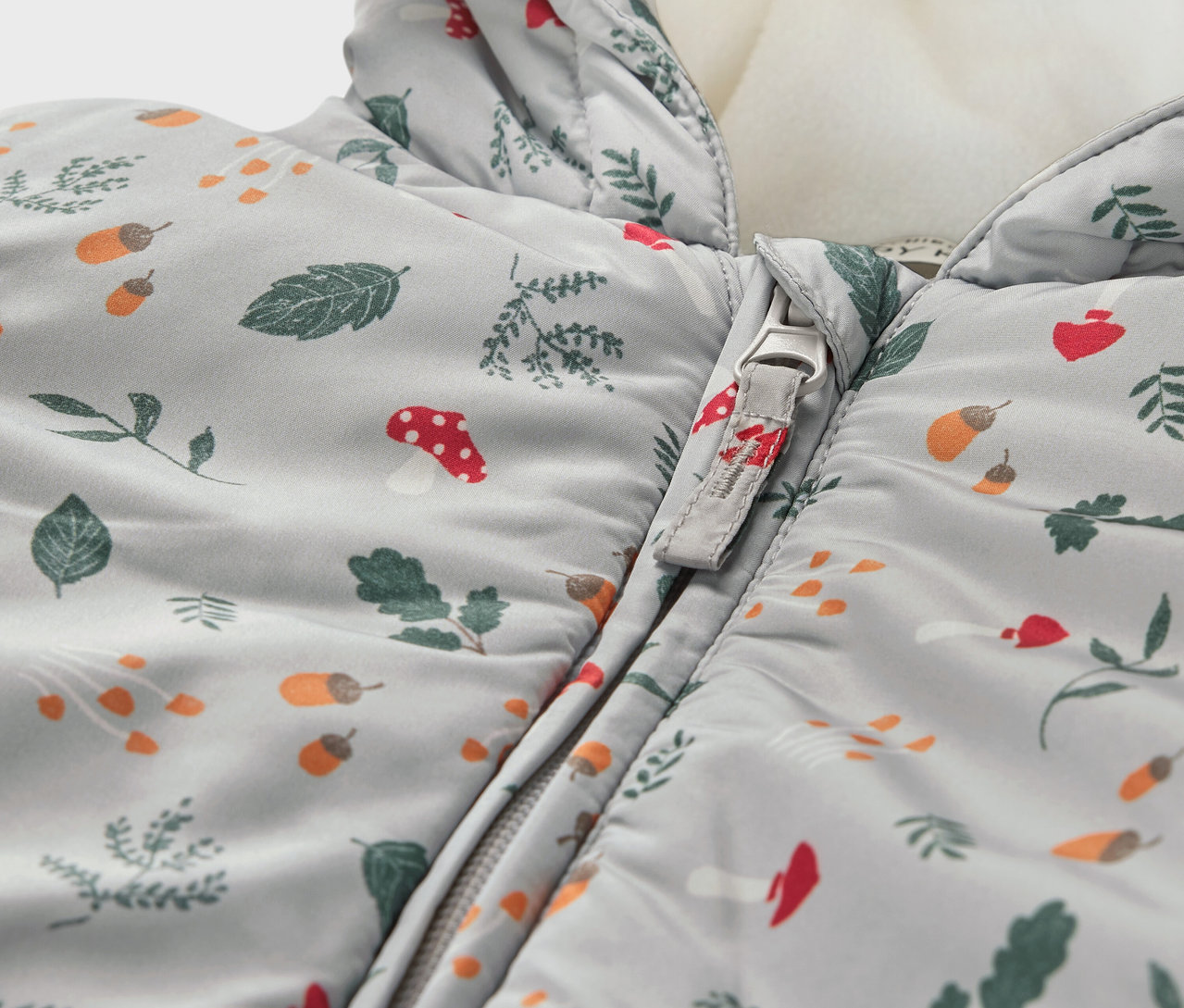 Detail zimného overalu pre bábätká so vzorom listov, húb a žalúdov.