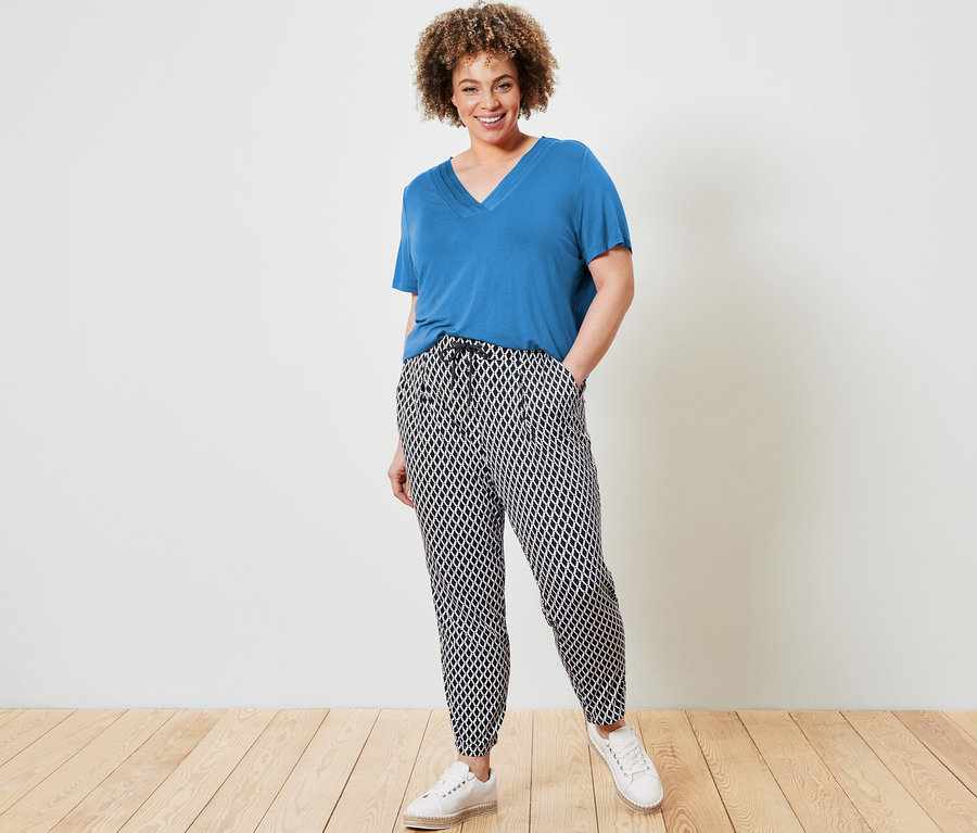Žena pózuje v kobaltovomodrom tričku so záhybom a džersejových nohaviciach s potlačou.