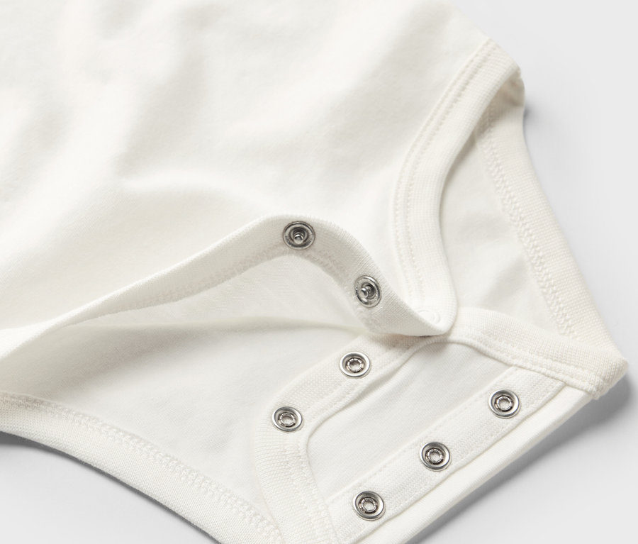 Detail bielych rastúcich body pre bábätká s patentkami.