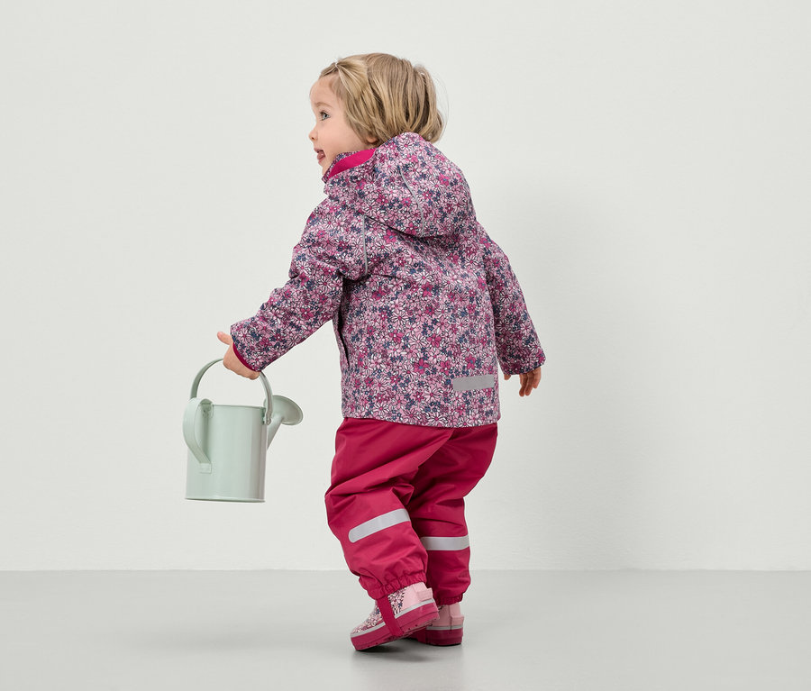 Dieťa v kvetinovej bunde a ružových nohaviciach drží kanvu.