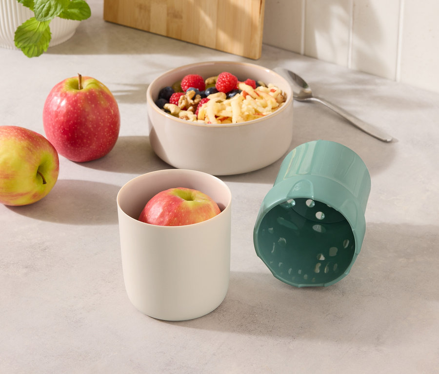 Dve jablká vedľa misky s müsli a pohára s jablkom a modrého pohára.