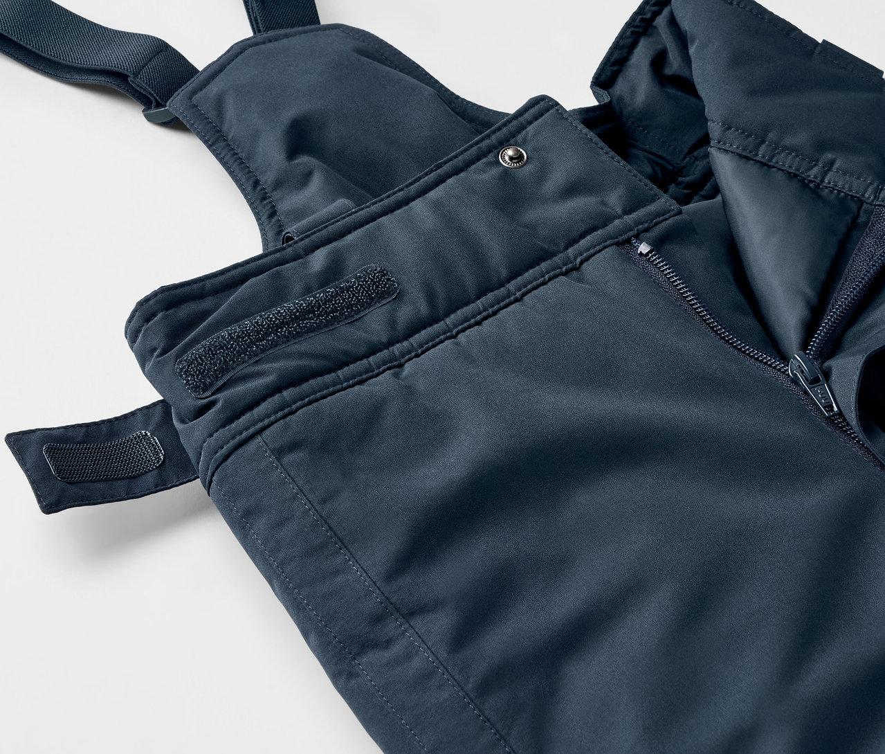 Detail modrých nohavíc s náprsenkou so zipsom a suchým zipsom.