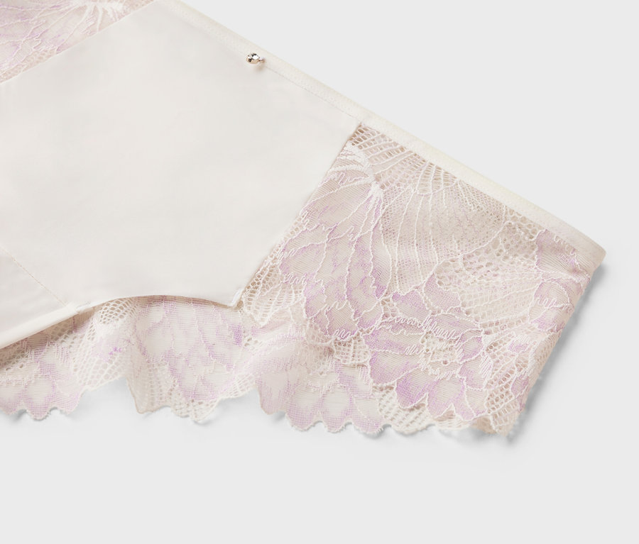 Detailný záber bielej podprsenky s fialovou čipkou na okrajoch na bielom pozadí.