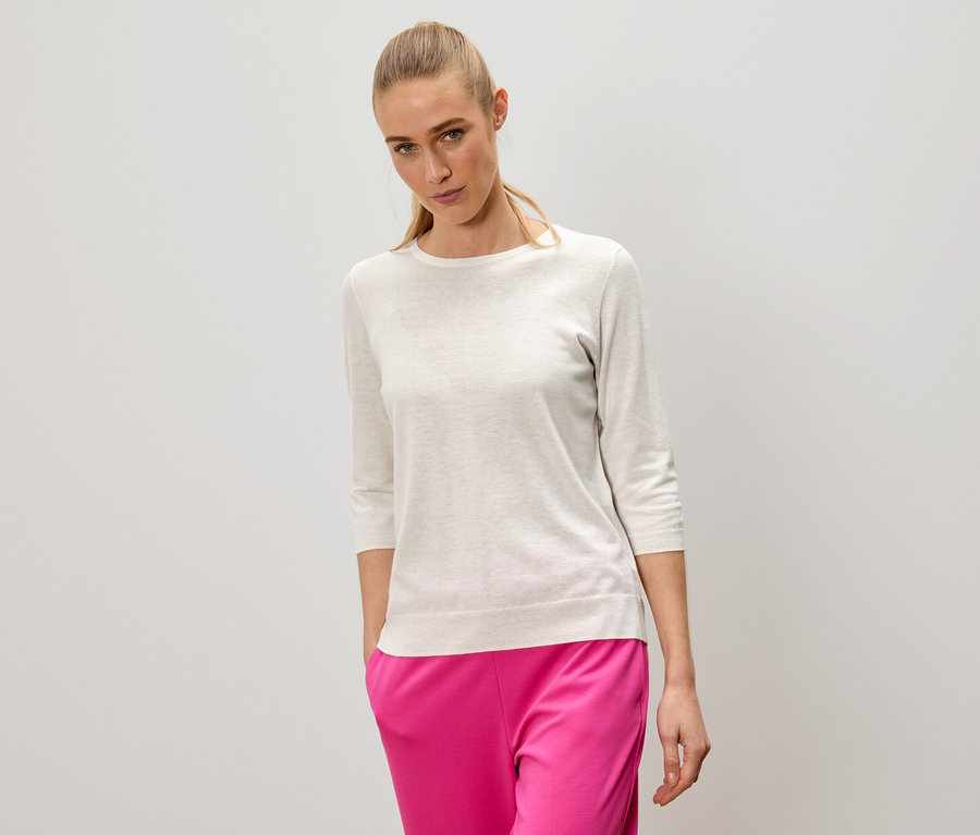 Žena s blond vlasmi má na sebe svetlý sveter a ružové nohavice.