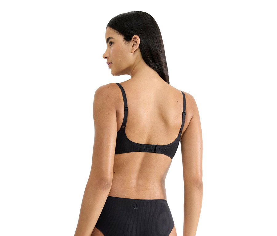 Pohľad zozadu na ženu s dlhými tmavými vlasmi, ktorá má na sebe čiernu podprsenku a spodnú bielizeň.