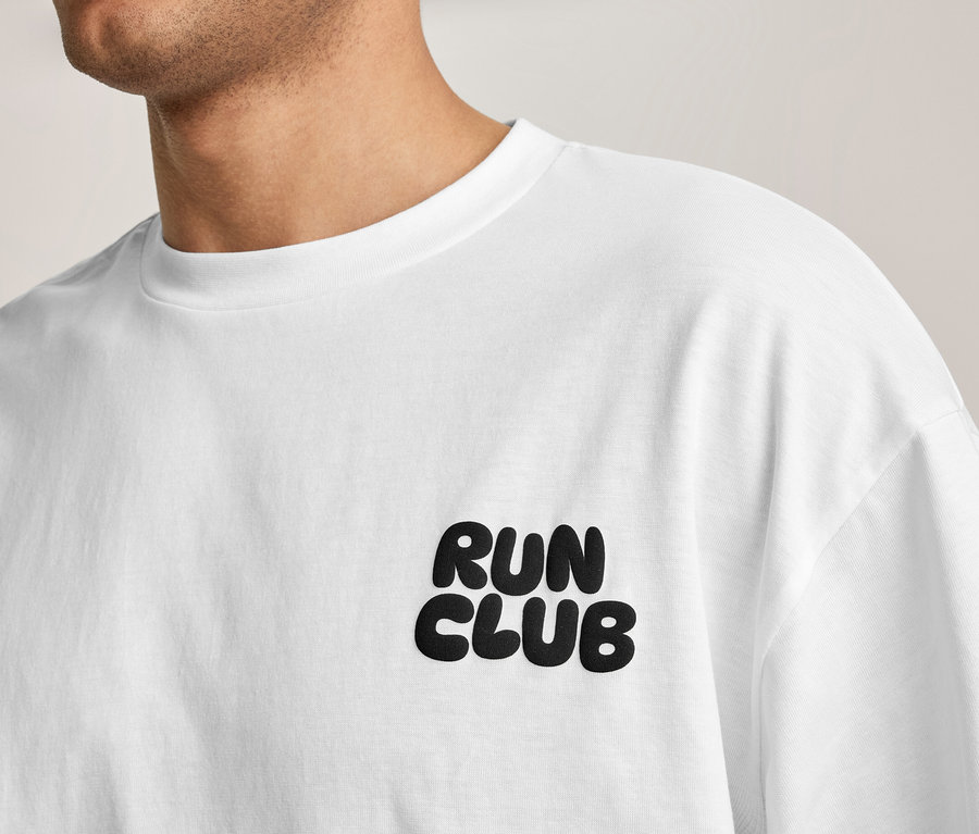Osoba má na sebe biele športové tričko s nápisom „RUN CLUB“ na hrudi.