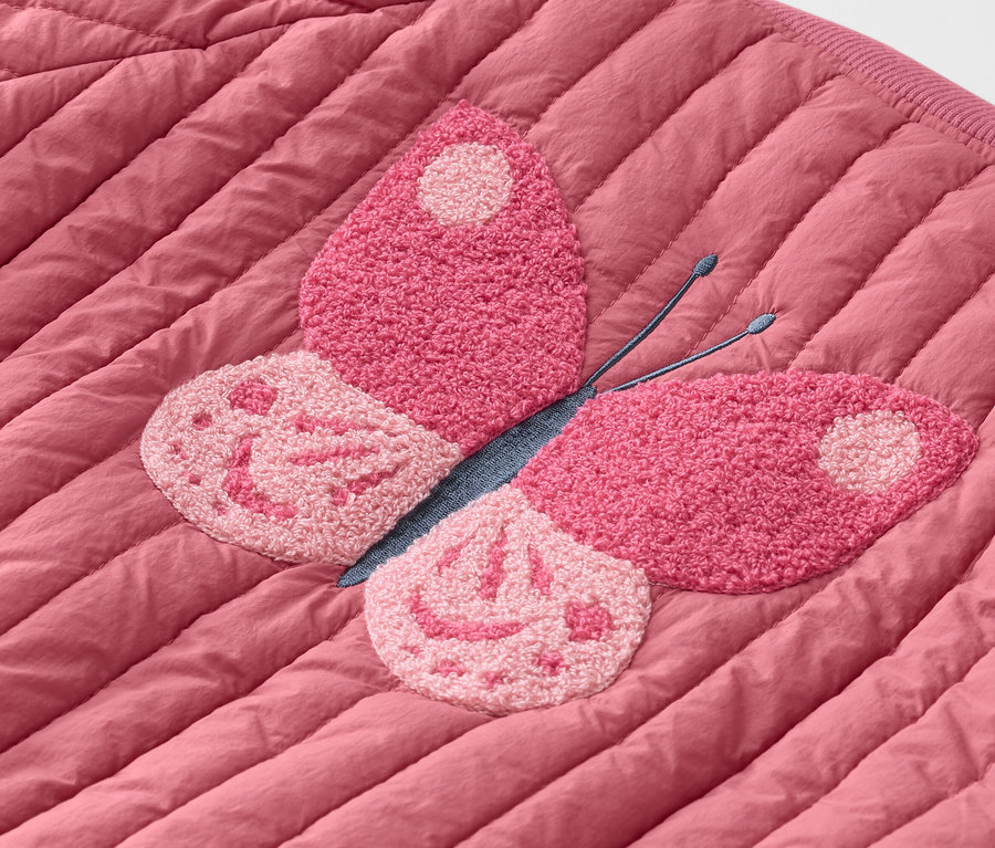 Detailný záber prešívanej ružovej bundy s ružovou nášivkou motýľa.