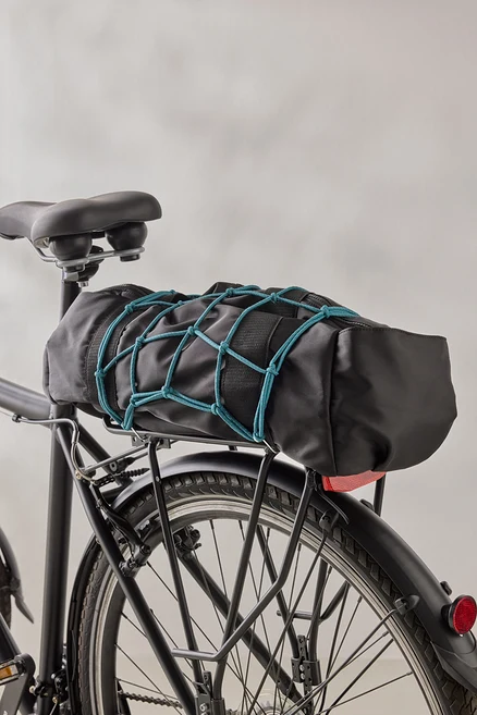 Čierna taška na bicykel je pripevnená k čiernemu nosiču bicykla pomocou modrej batožinovej siete.