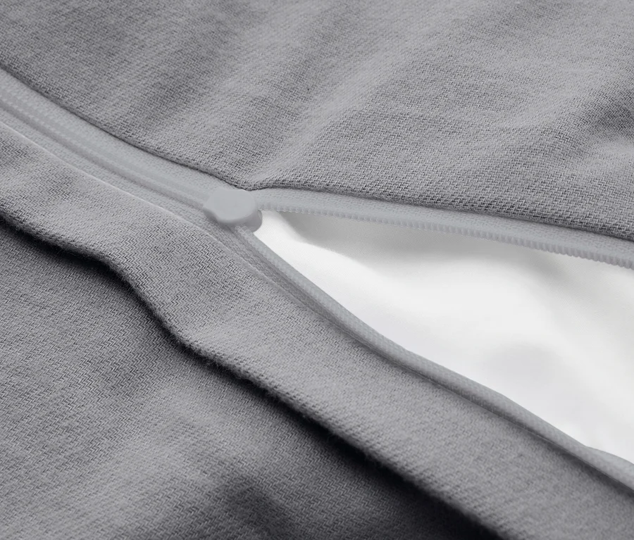 Detail sivého materiálu s čiastočne otvoreným svetlosivým zipsom, ktorý odhaľuje biely materiál pod ním.
