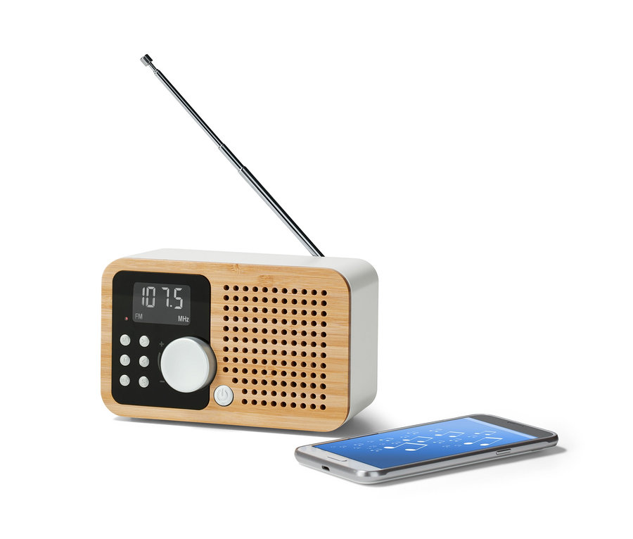 Kompaktné FM rádio »Bambus« s vysunutou anténou stojí vedľa smartfónu.