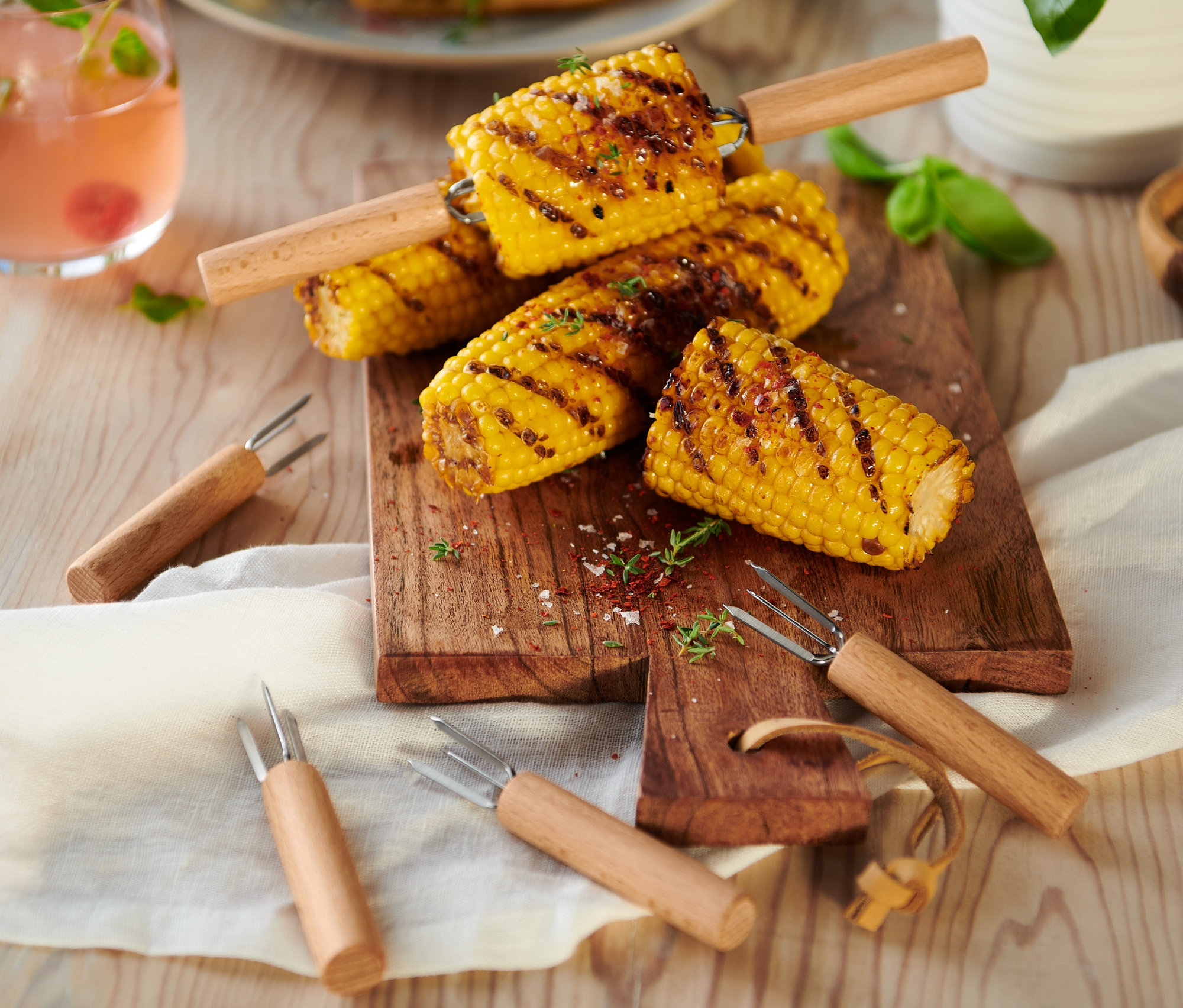 Grilovaná kukurica na drevenej doske s 8 držiakmi na kukuricu.