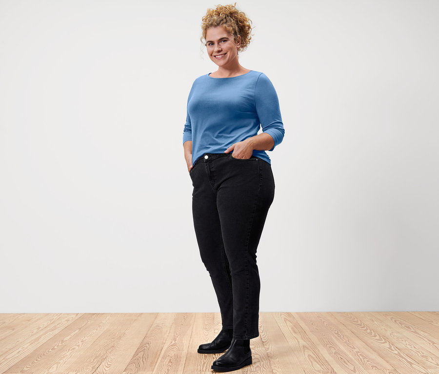 Žena stojí a pózuje v svetlomodrom tričku s trojštvrťovými rukávmi.