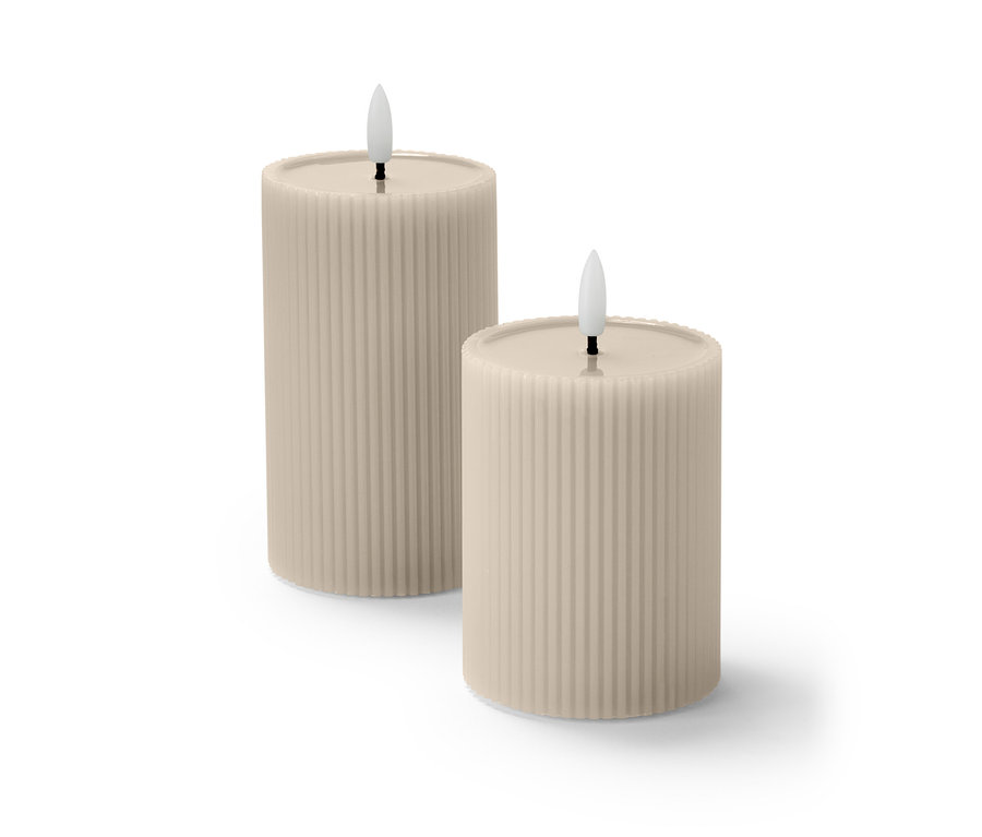 Dve béžové LED sviečky s výplňou zo skutočného vosku a vrúbkovaným povrchom stoja vedľa seba.