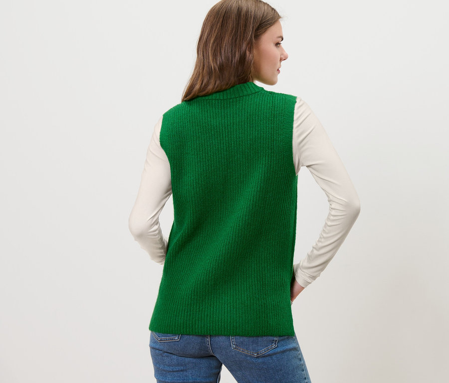Žena pózuje chrbtom v zelenej pletenej veste.