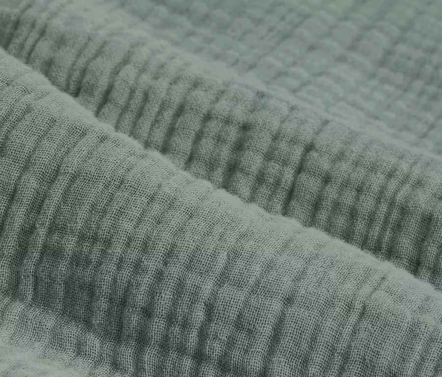 Detailný záber na zelenú mušelínovú posteľnú bielizeň štandardnej a nadmernej veľkosti.