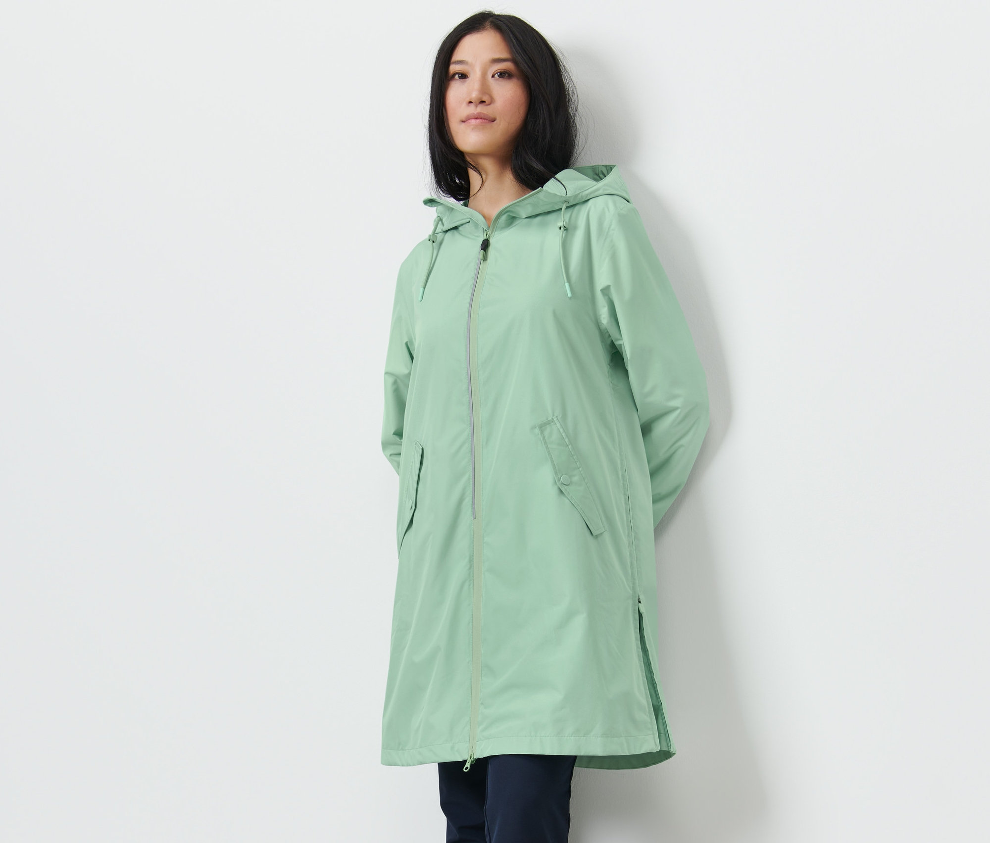 Žena pózuje v kabáte do dažďa svetlozelenej farby.