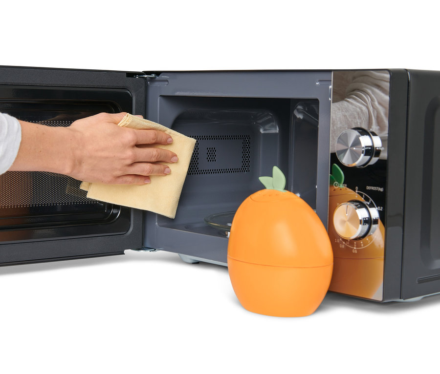 Ruka utiera vnútro mikrovlnnej rúry handričkou vedľa čističa mikrovlnnej rúry v tvare pomaranča.