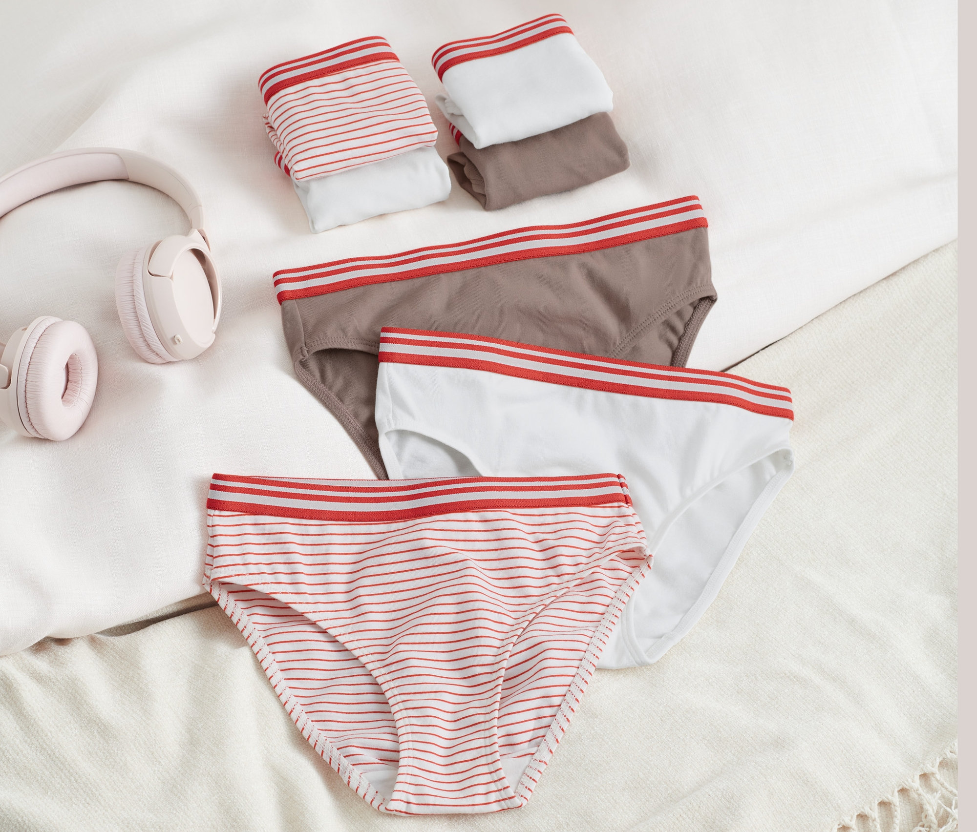 Na posteli ležia dievčenské nohavičky, 7 ks, s prúžkami, hnedé a biele, vedľa slúchadiel.