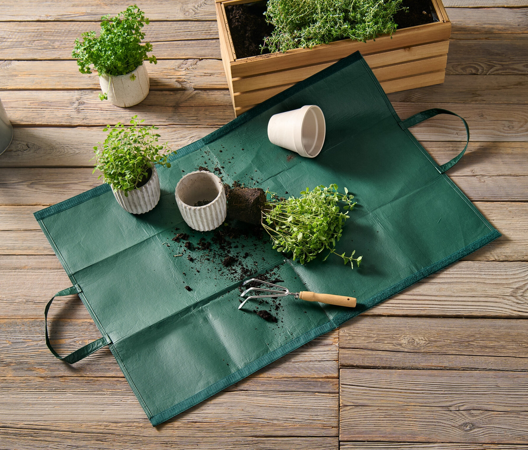 Záhradná taška na odpad leží na drevenej podlahe vedľa črepníkových rastlín a kanvy.
