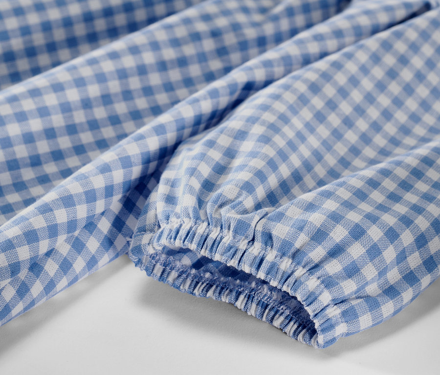 Detail detských tkaných šiat s modro-bielym kockovaným vzorom a dlhým rukávom.