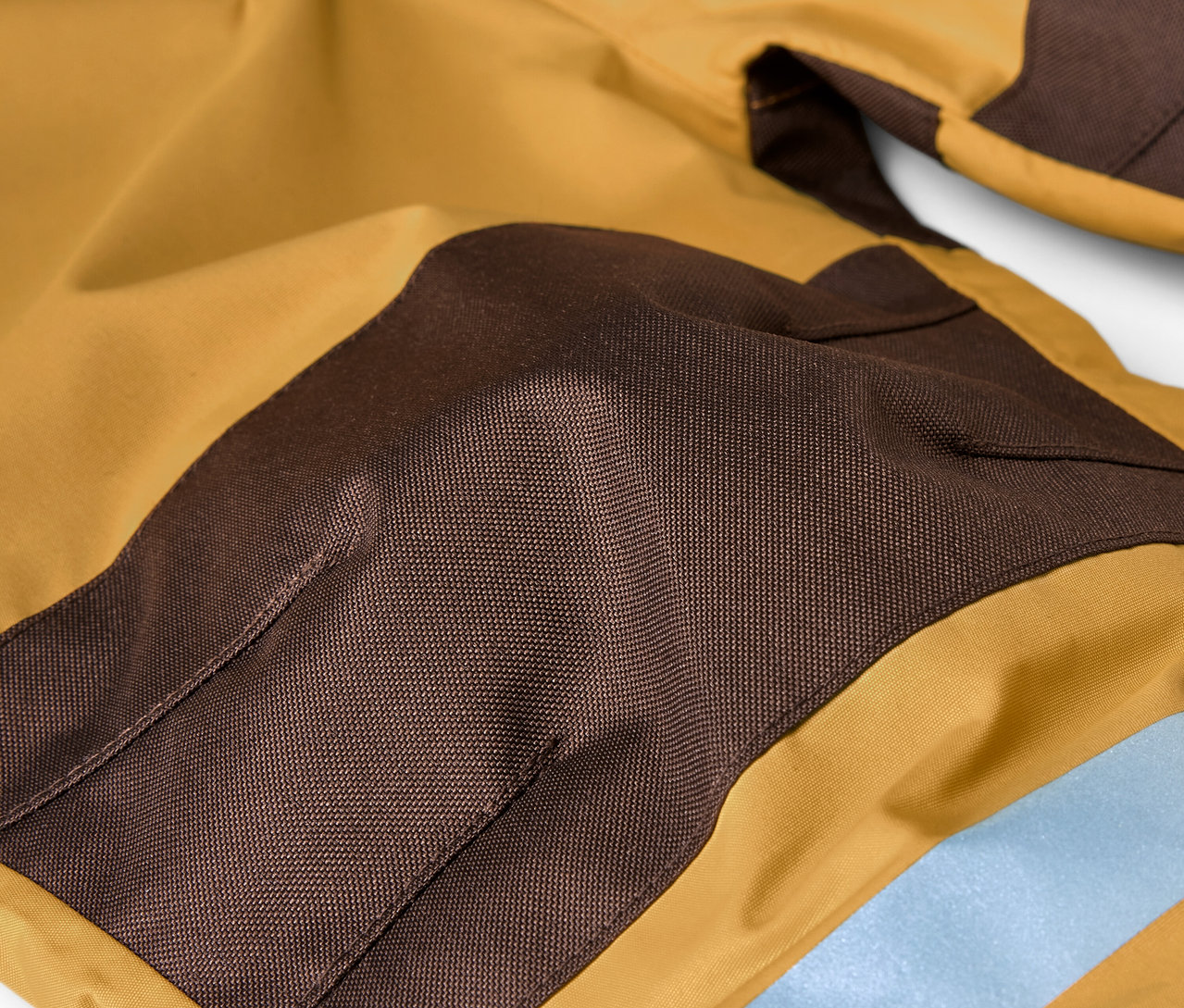 Detail detskej kombinézy do dažďa v hnedej a okrovej farbe.