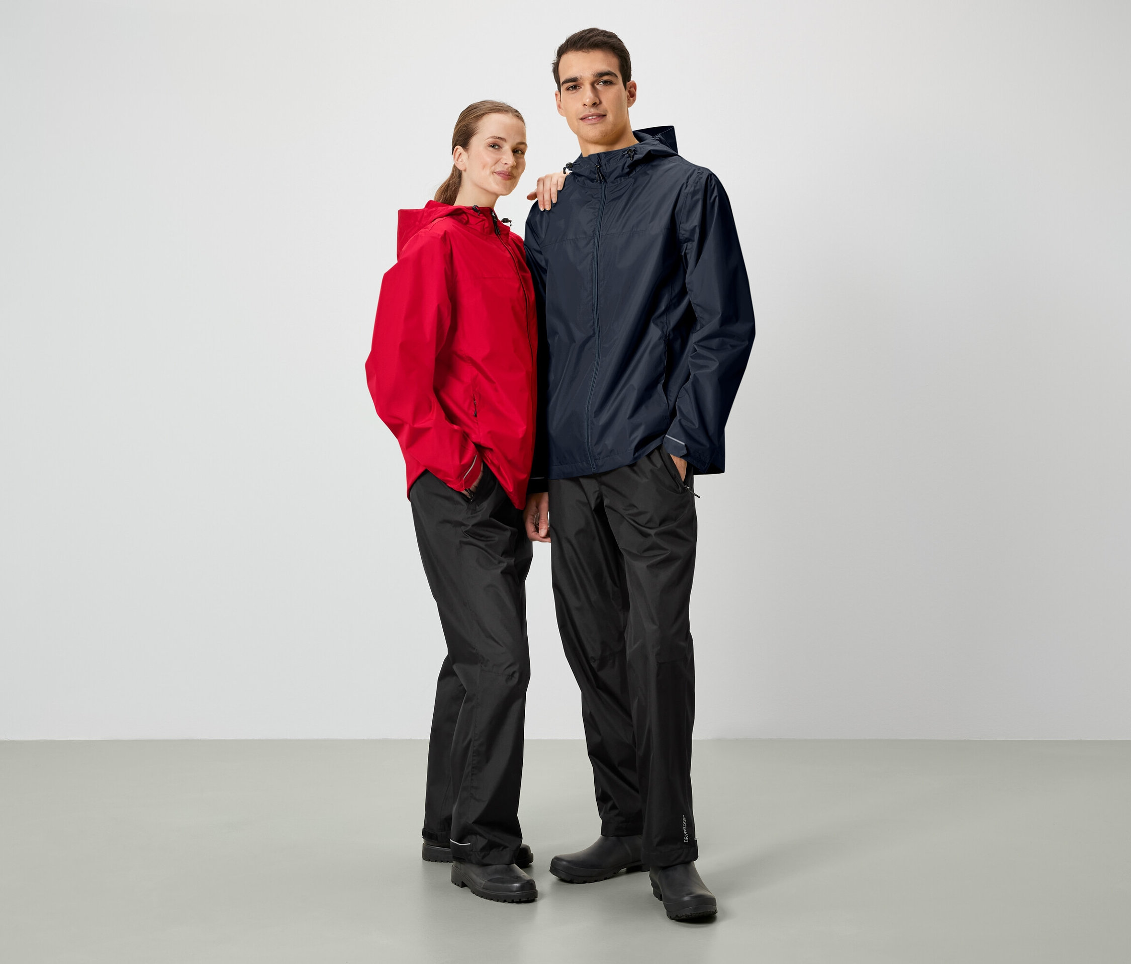 Muž a žena pózujú vedľa seba. Obaja majú na sebe bundy do dažďa a čierne nohavice.